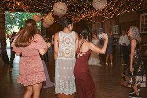 People dancing at a wedding reception under warm string lights and paper lanterns.