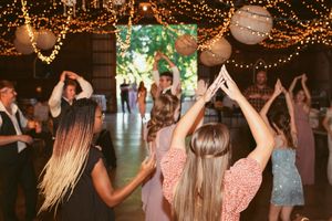 People dancing with their arms raised under twinkling string lights at a festive celebration.