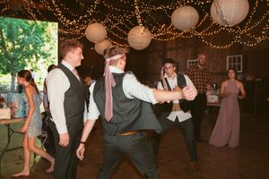 People dance and celebrate at a rustic barn reception venue decorated with twinkling string lights.