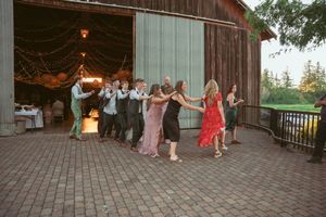 Dancing couples twirl across a wooden deck outside a rustic barn venue during sunset.
