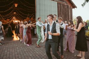Wedding celebration outside a rustic barn with string lights and dancing guests at dusk.