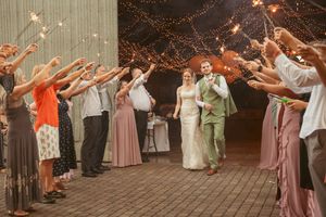 Wedding guests form an archway with raised arms as couple walks underneath at outdoor reception with string lights.