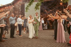 Wedding guests form an exit line on brick pavement outside a rustic barn venue.