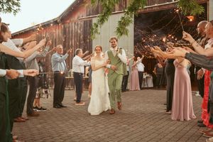 A couple walks through a tunnel of guests during their wedding exit at a rustic barn venue.