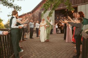 Wedding party and guests form lines for an outdoor celebration near a rustic barn.