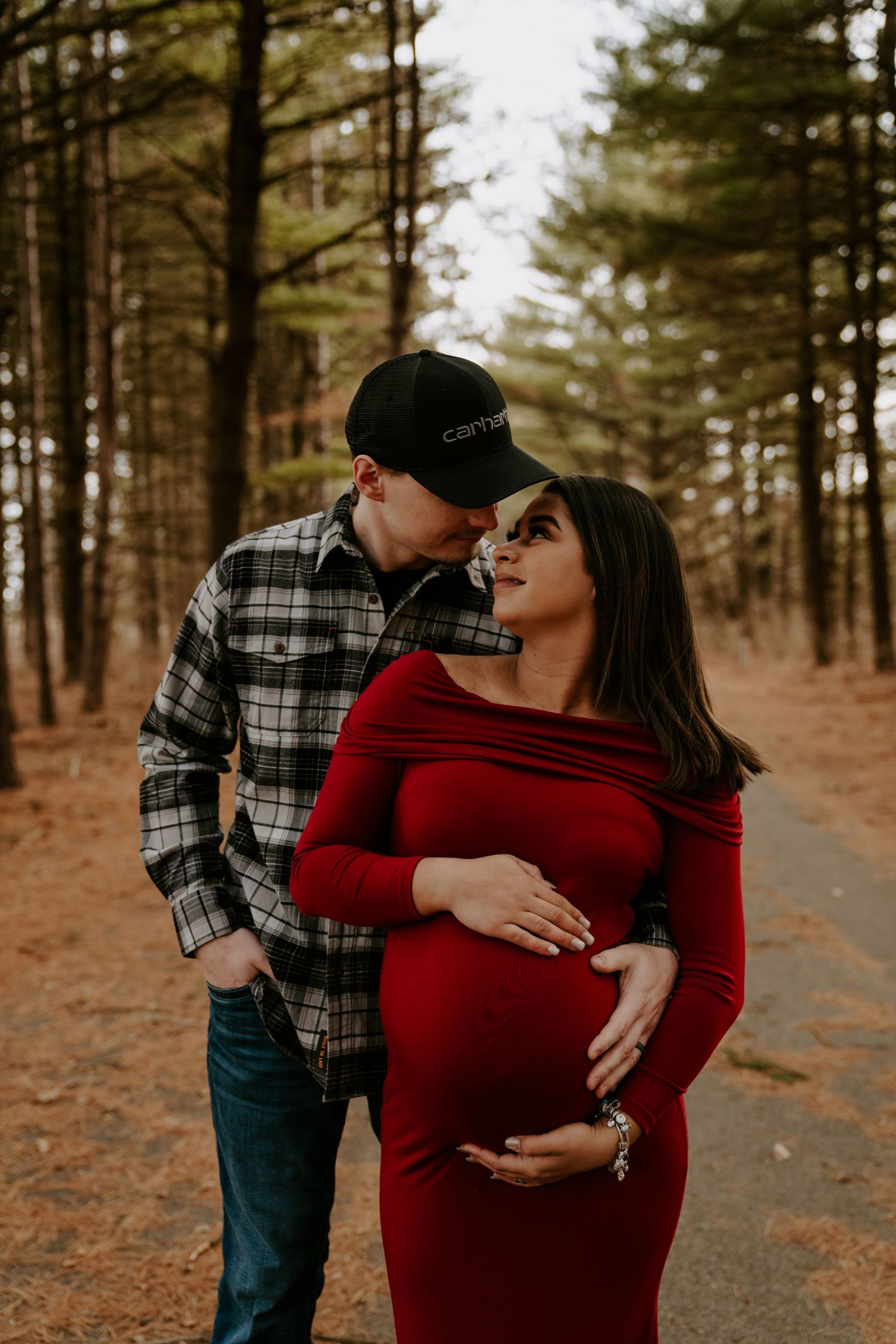 A couple shares an intimate moment in a pine forest wearing red and plaid.