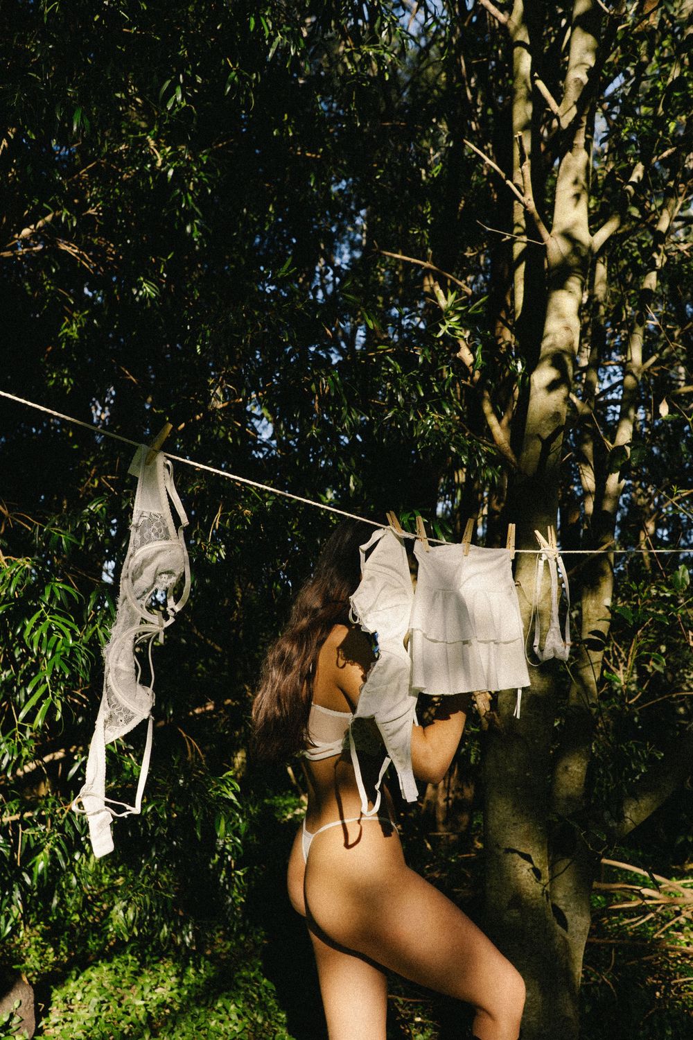 Laundry hanging on a clothesline between trees in a backyard with green foliage in the background.