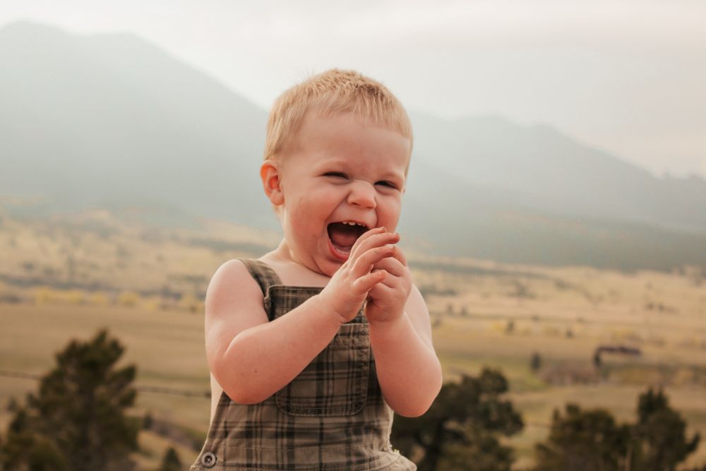 A small child sits in a brown field looking thoughtfully into the distance on a cloudy day |Westminster Family Photographer