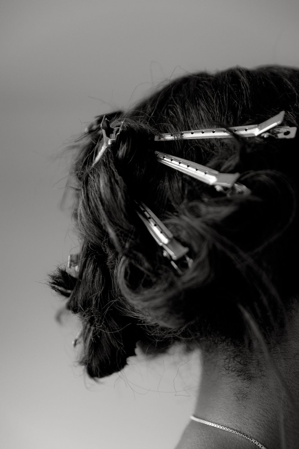 A series of black and white photos showing hair clips and bobby pins holding up dark hair in a minimalist style.