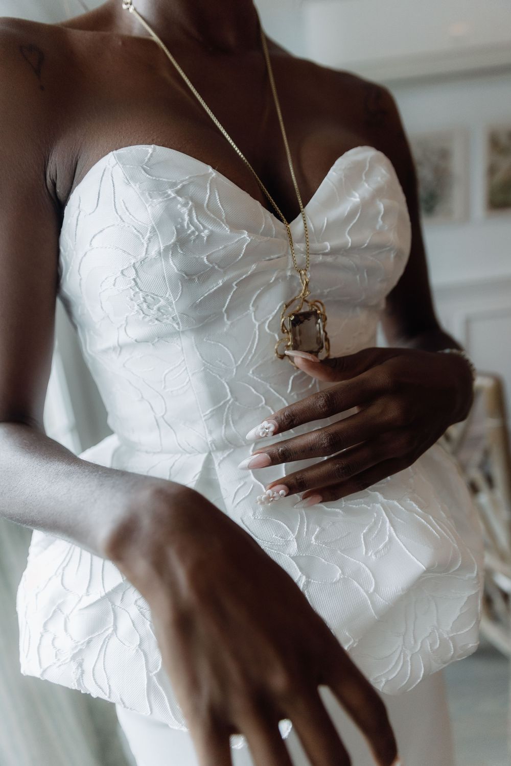 Close-up detail of a white strapless wedding dress with embroidered pattern and delicate necklace pendant.
