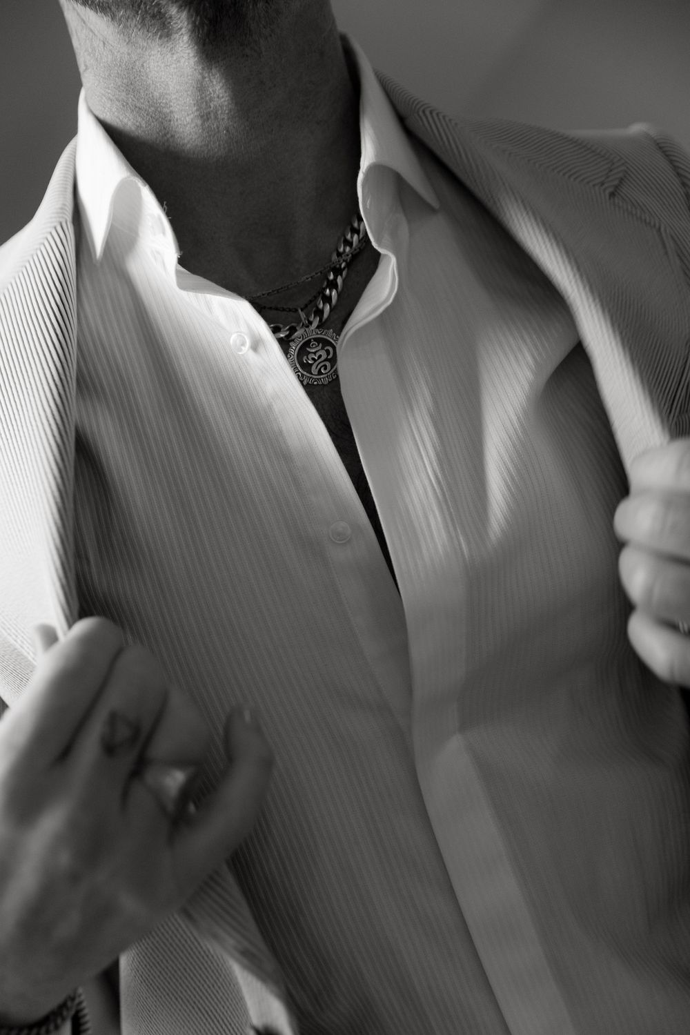 Close-up black and white photo of a formal white dress shirt with textured fabric and decorative chain detail at collar.