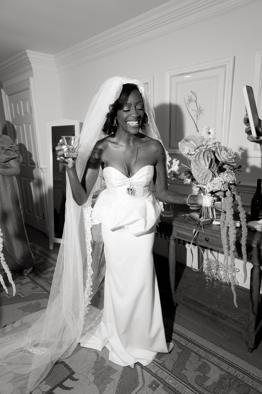 Black and white photo of a bride in a flowing white gown preparing in an elegant room.