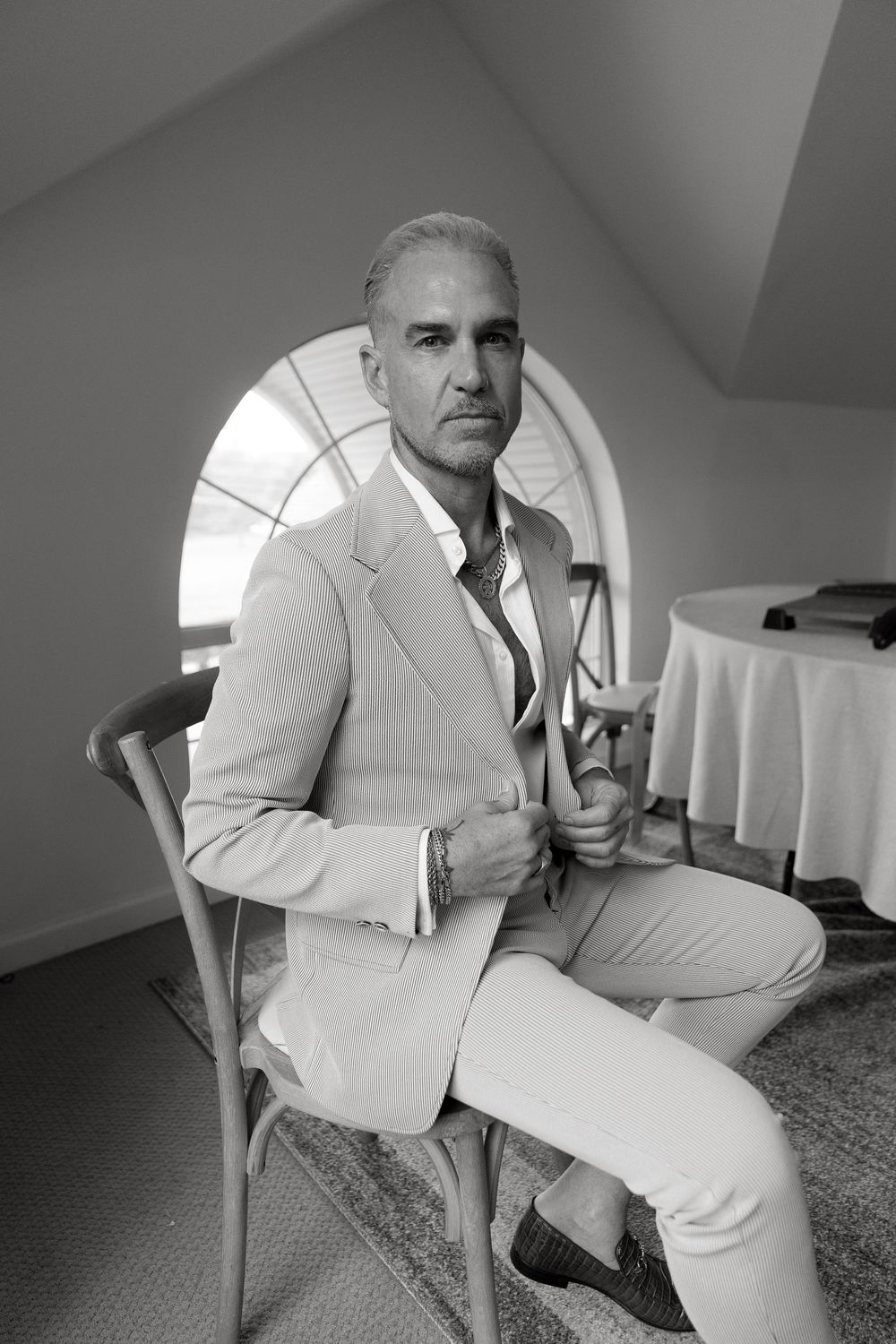 A series of black and white portraits showing someone posing in a light-colored suit and chair.