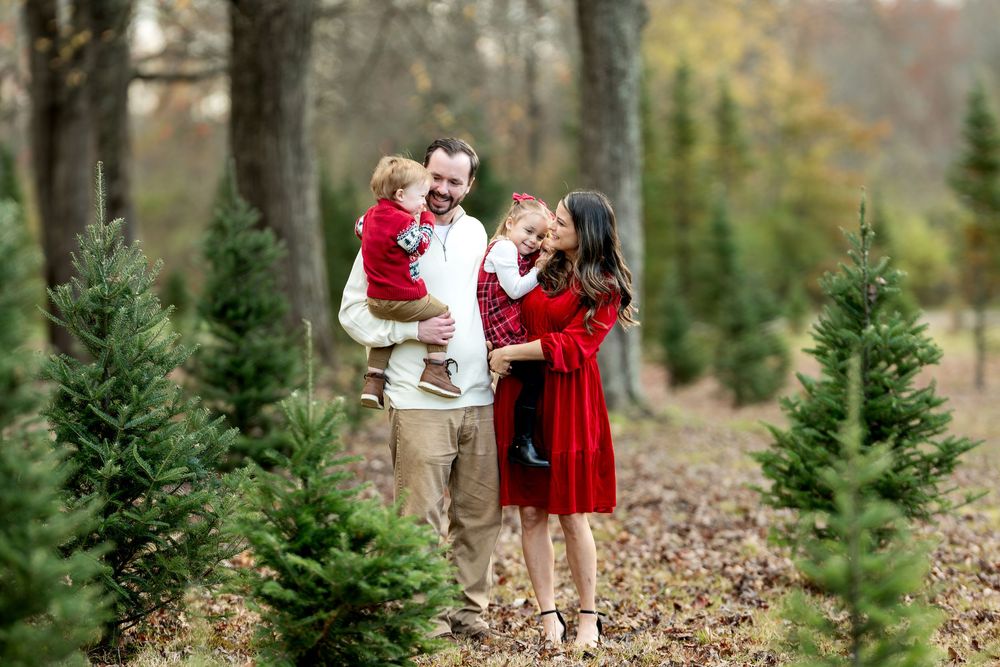 Happy family laughing together at a Christmas tree farm, dressed in coordinating red holiday attire.