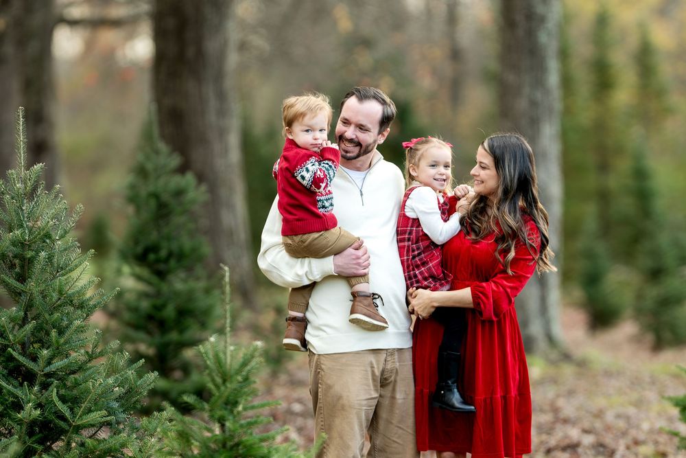 Smiling family of four enjoys a Christmas tree farm photoshoot in matching red and plaid outfits.