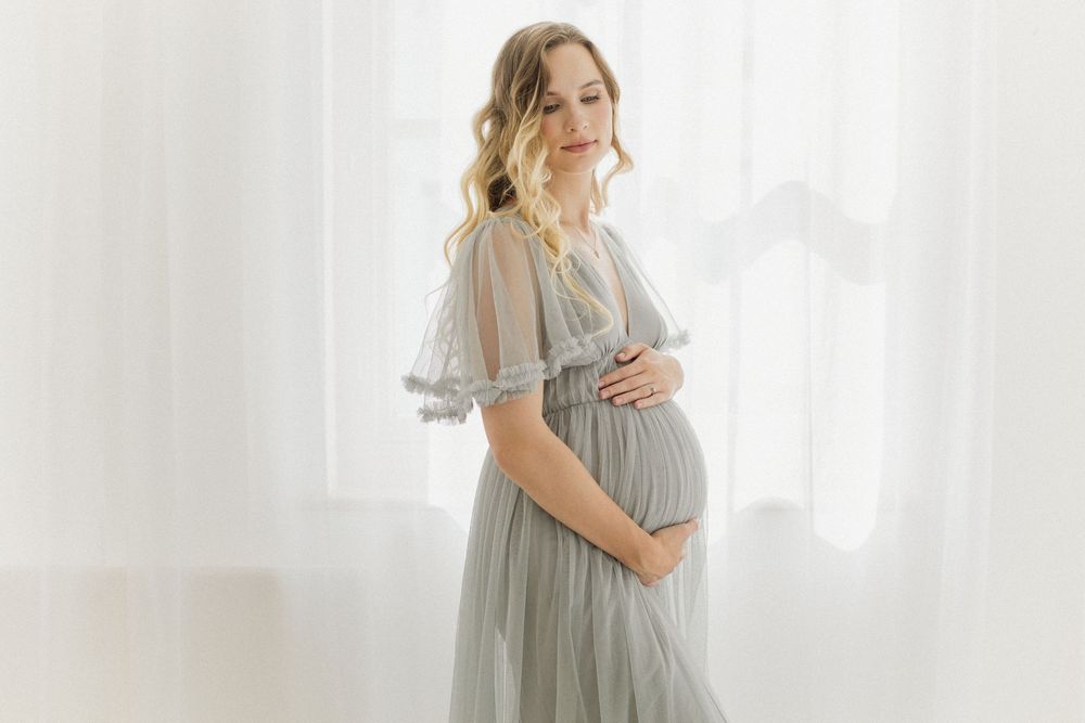 Maternity portraits in flowing grey dress against bright white background.
