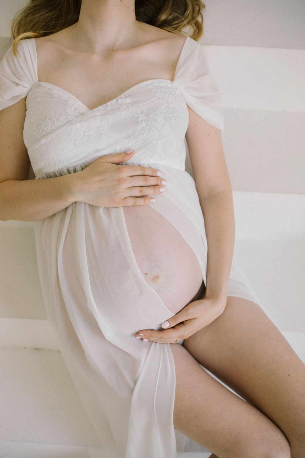 Intimate maternity boudoir photo featuring soft white fabric draping over a pregnant figure.