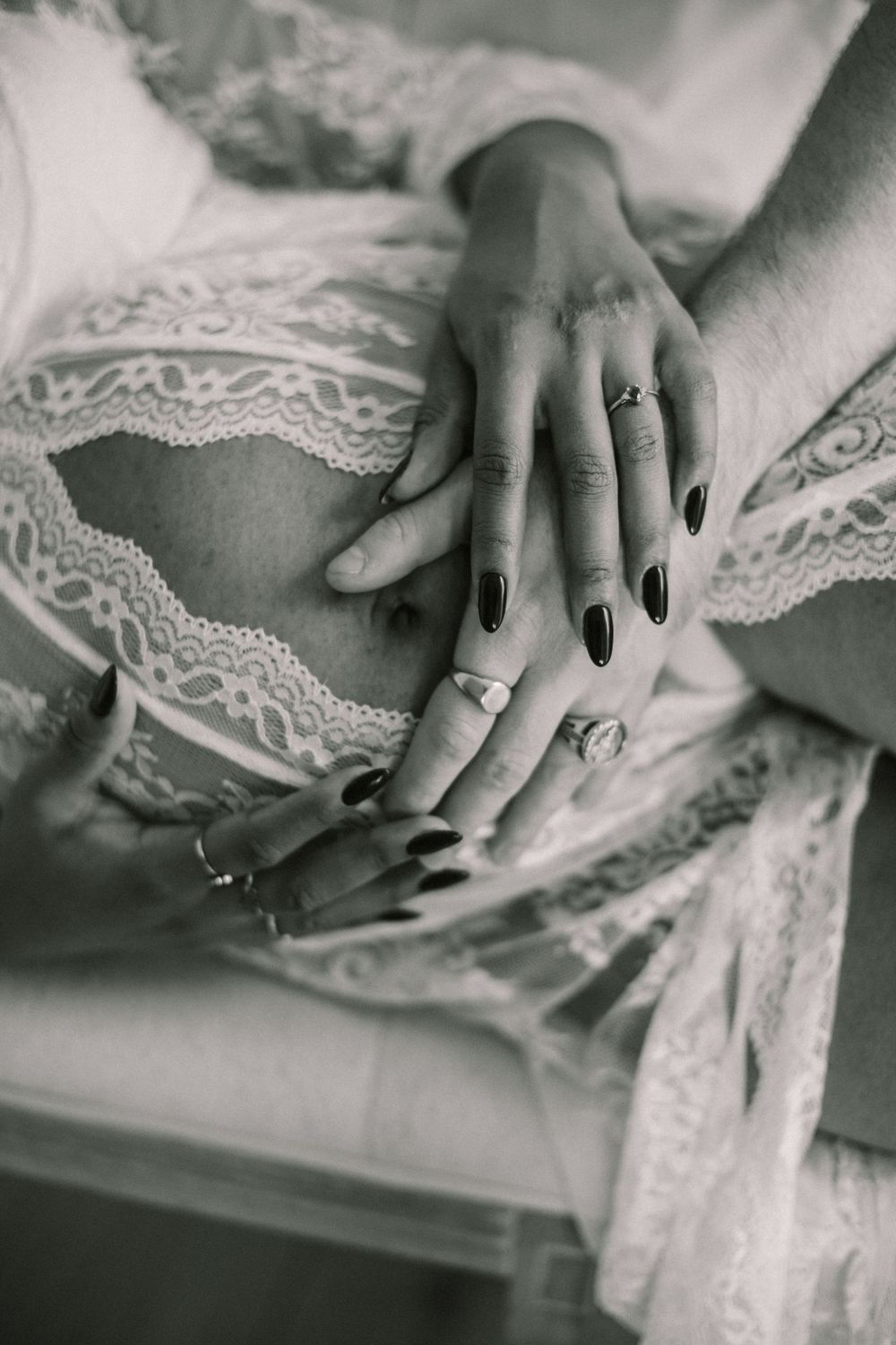 Close-up black and white photos of a pregnant woman holding husband hands that gently hold her baby bump
