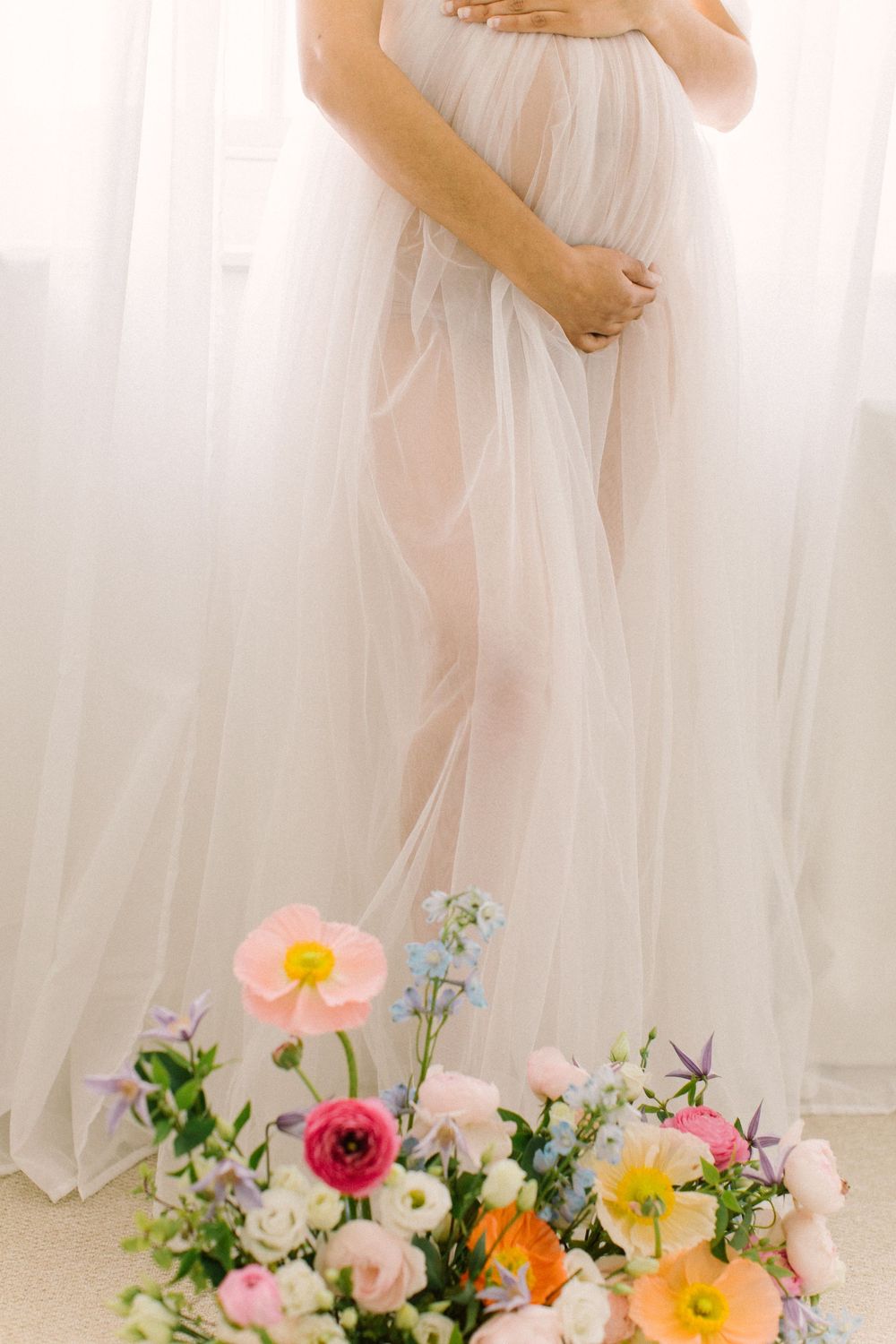 Ethereal maternity portrait with flowing white dress and colorful floral arrangement.
