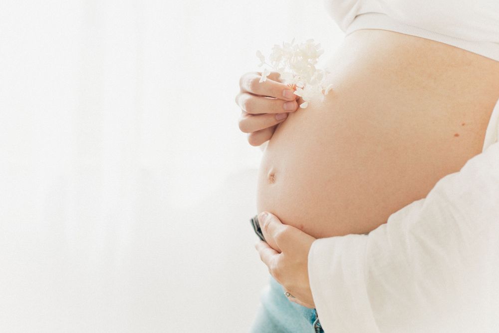 Side view of pregnant belly being gently cradled against light background.