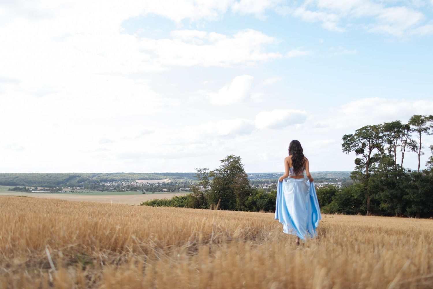 Femme en robe bleue marchant dans un champ doré au coucher du soleil, photo naturelle et poétique.