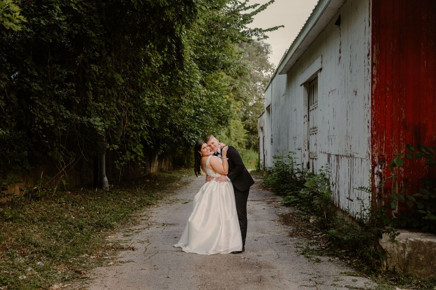 A romantic wedding photo series showing a couple walking down a rustic path near a white and red barn.