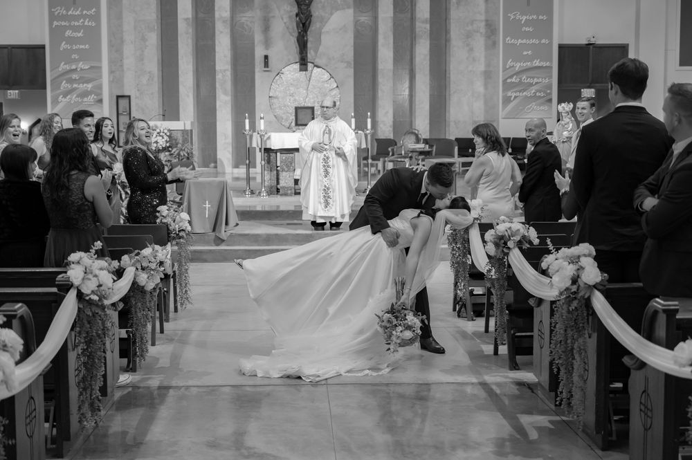 Black and white church ceremony photo with decorated aisle and gathered congregation.