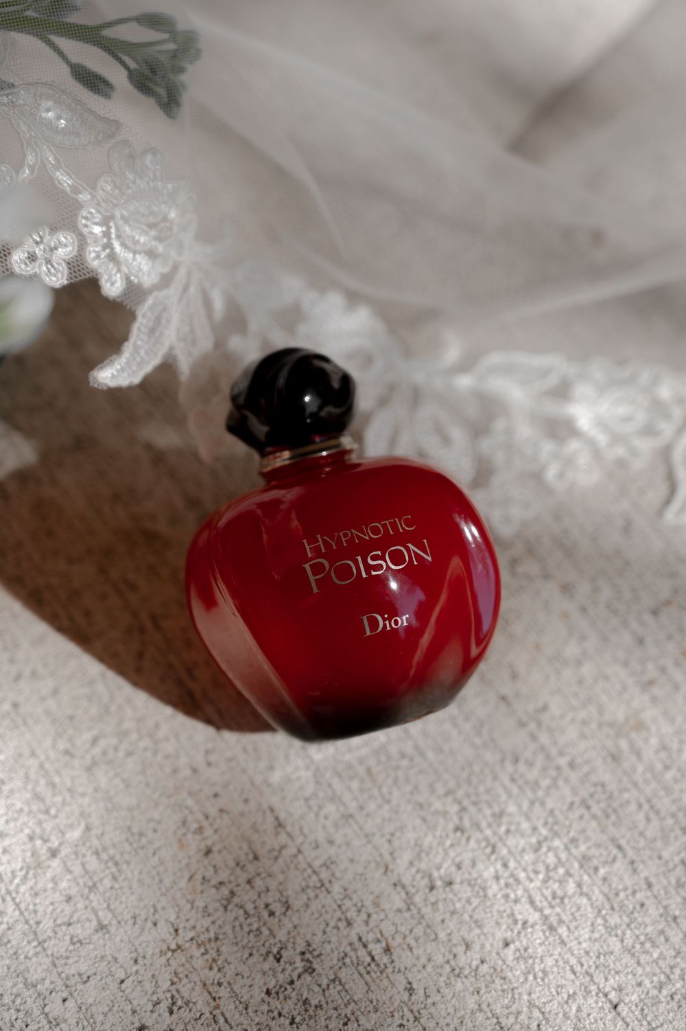 Red Dior Hypnotic Poison perfume bottle on white lace fabric.