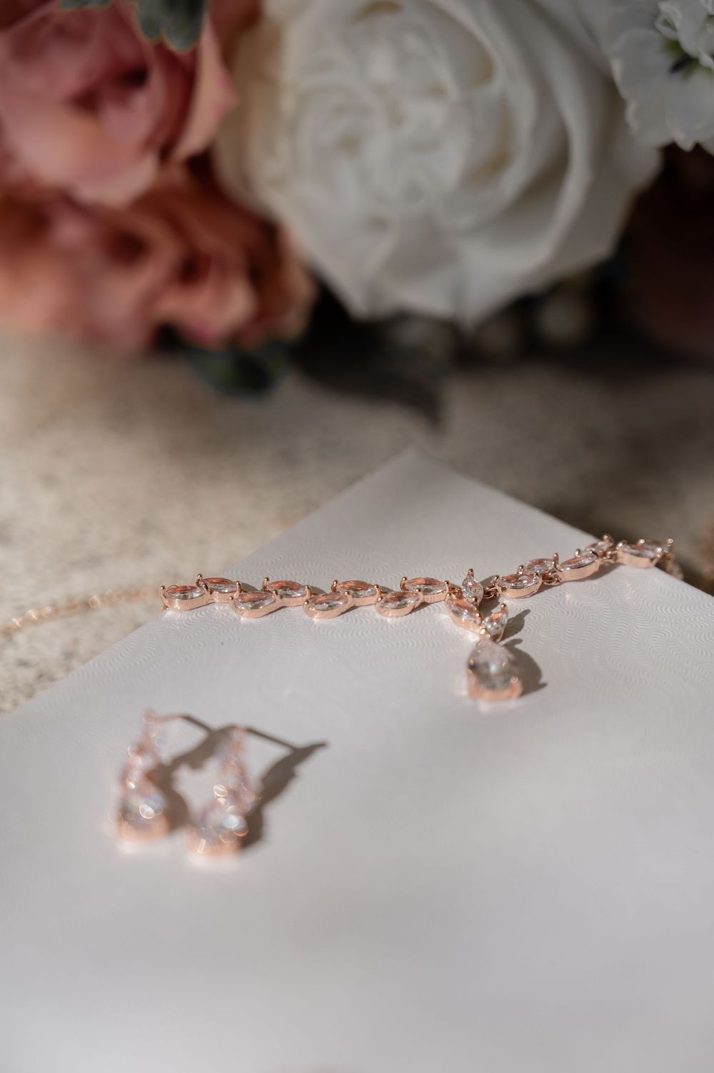 Rose gold wedding jewelry with crystal earrings and bracelet on white surface.