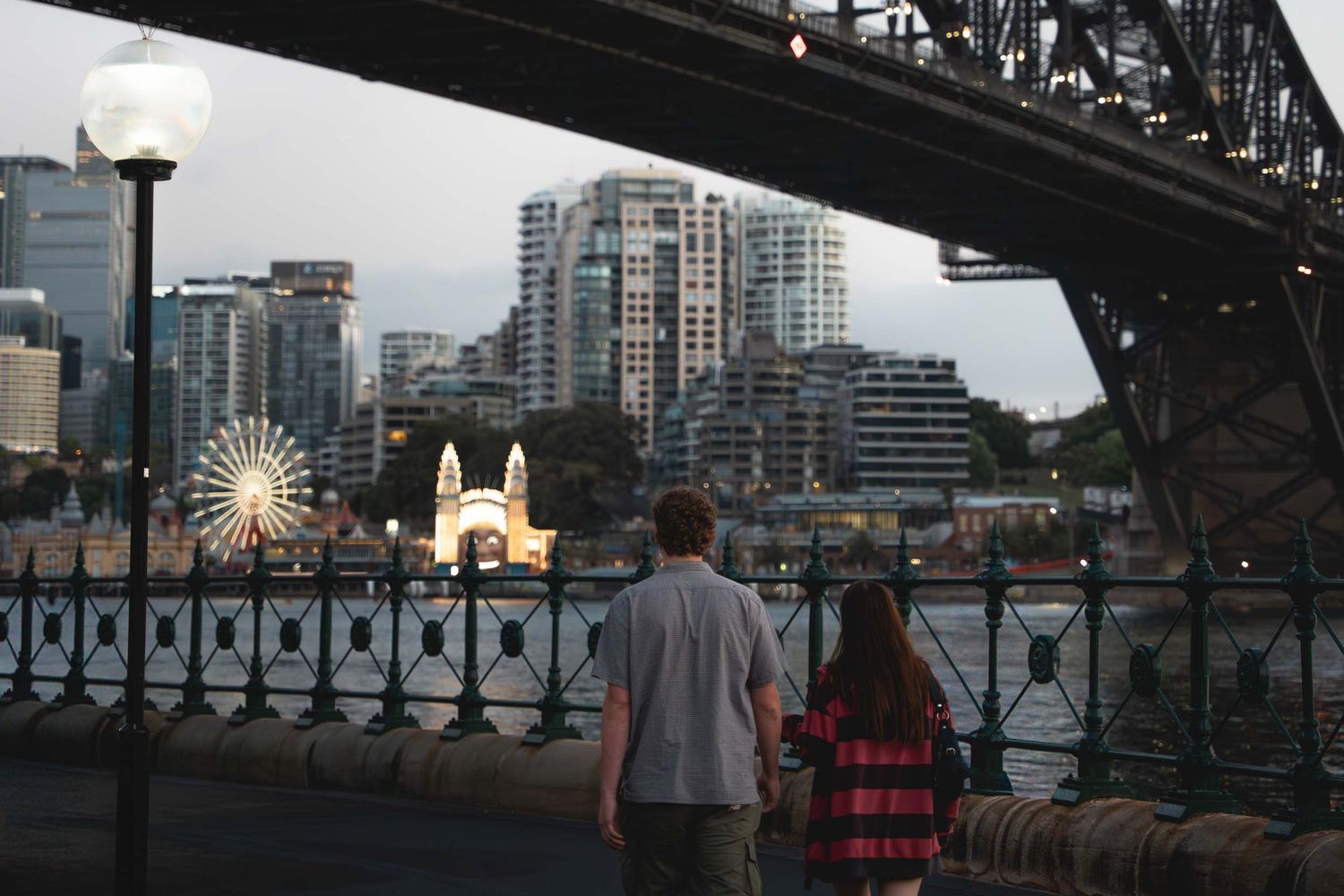 Young coupke in Sydney walking under the Sydney Harbour bridge during sunrise, Luna park in the background.