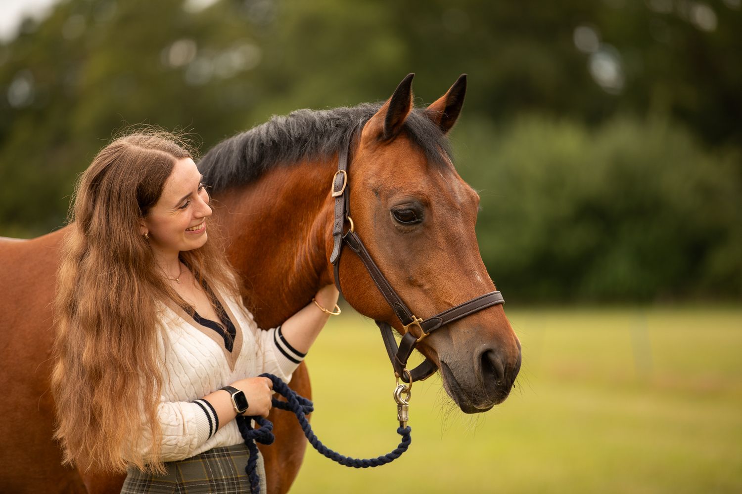 A group poses with horses along a tree-lined path during a sunny autumn day for outdoor photos.