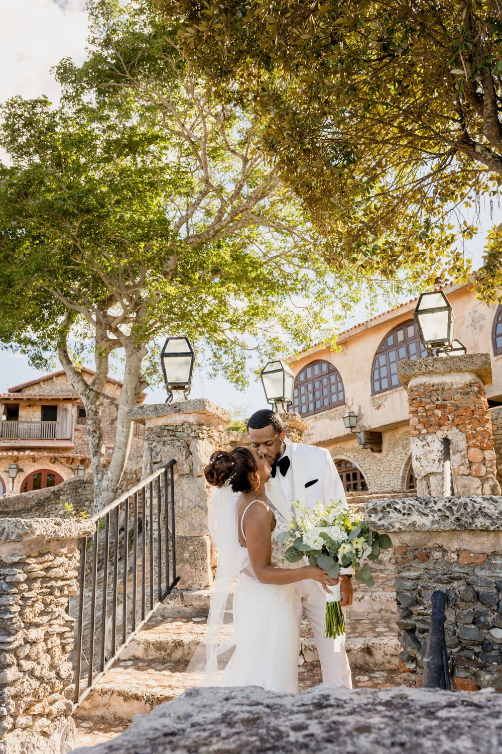 A romantic wedding photo series showing a couple embracing on stone steps at a rustic venue with arched architecture.