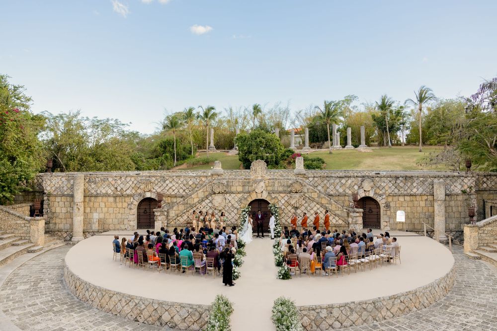 Aerial view of guests seated at outdoor amphitheater wedding venue with stone archways and tropical landscaping.