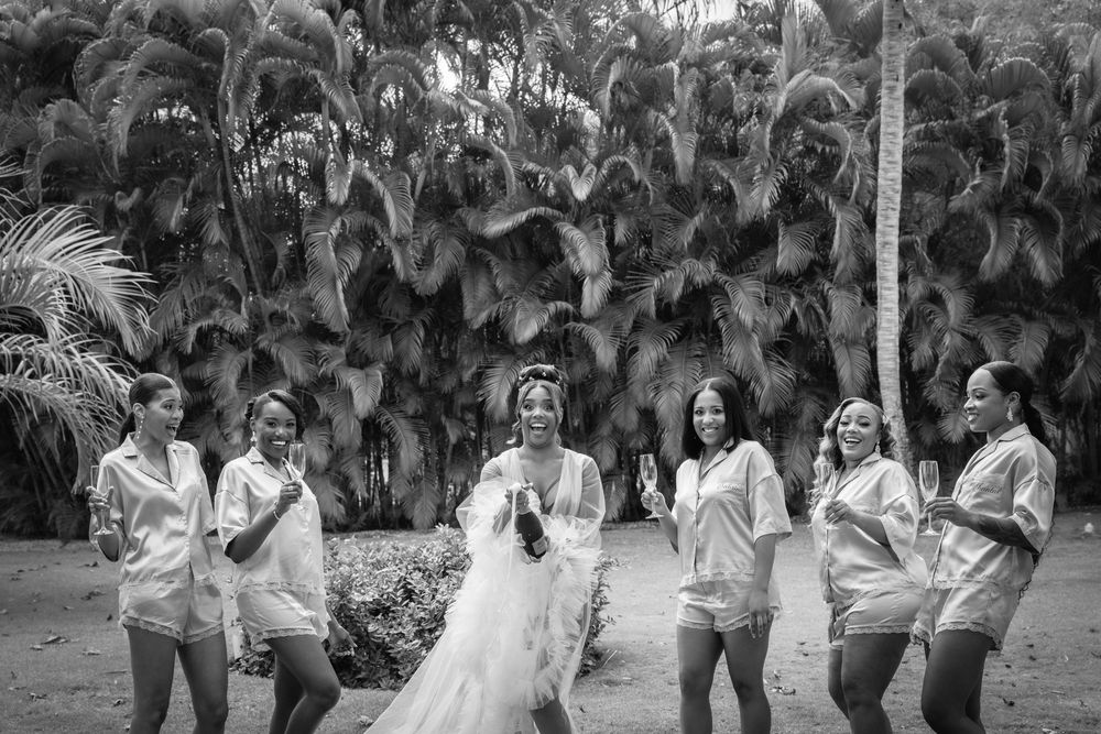A group of people dancing together outdoors in a tropical garden setting with palm trees in the background.