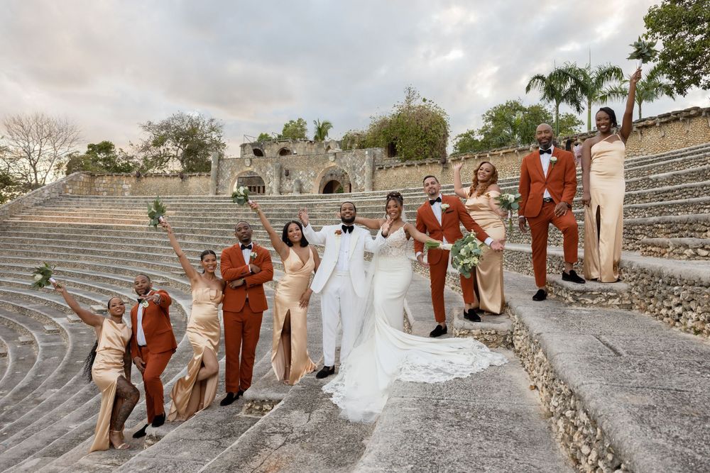 Wedding party in formal attire walking and posing on stone steps outdoors with palm trees in the background.