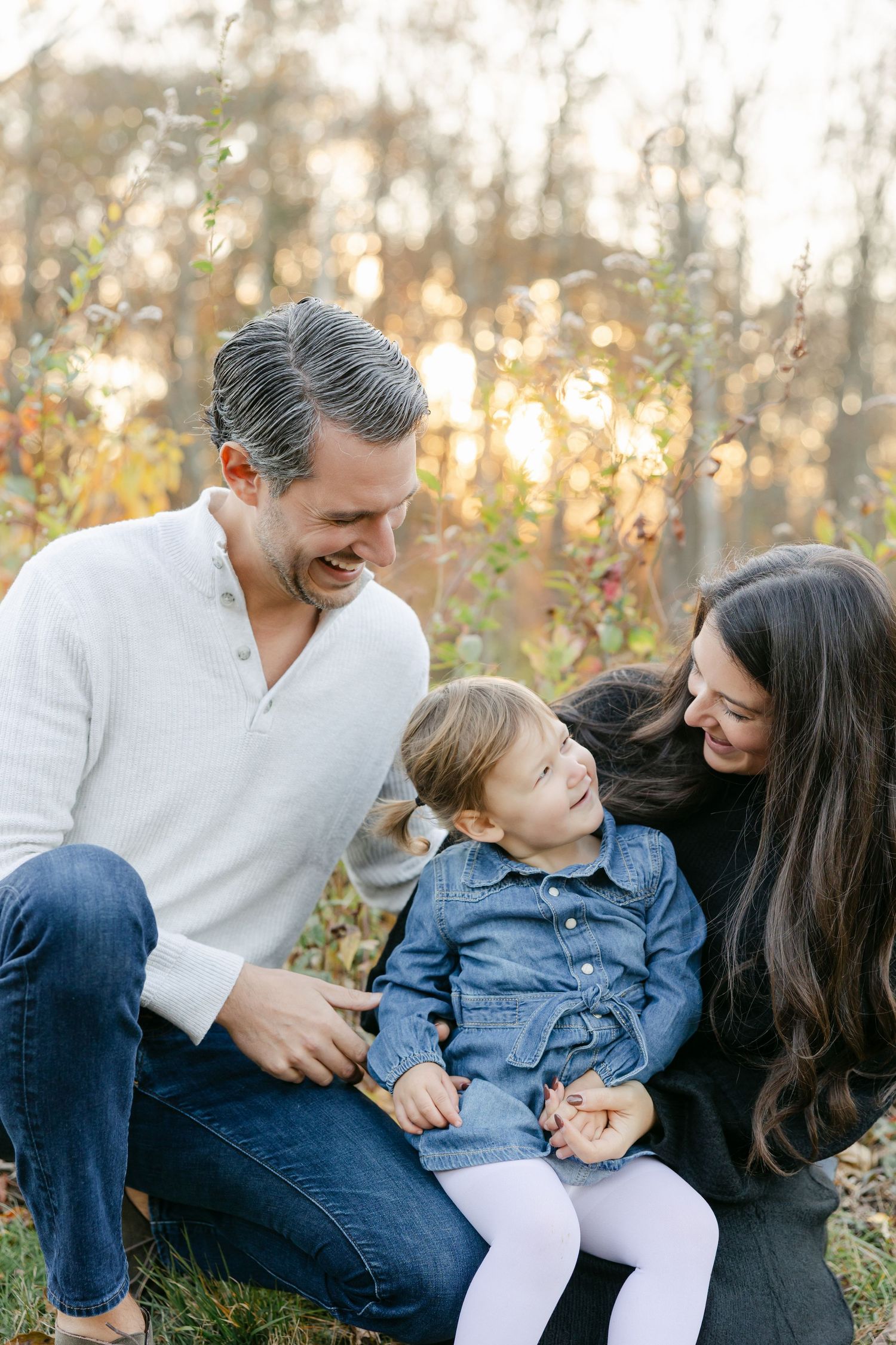 Family sharing playful moments together on grass during sunset.