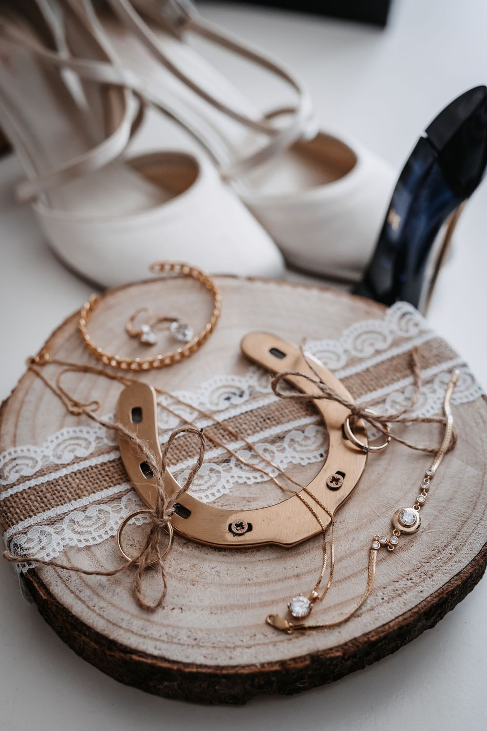 Wedding rings and accessories arranged on rustic wood slice with lace and twine details.