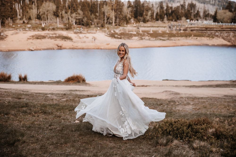 Wedding couple walks along a scenic beach shoreline in flowing white attire.