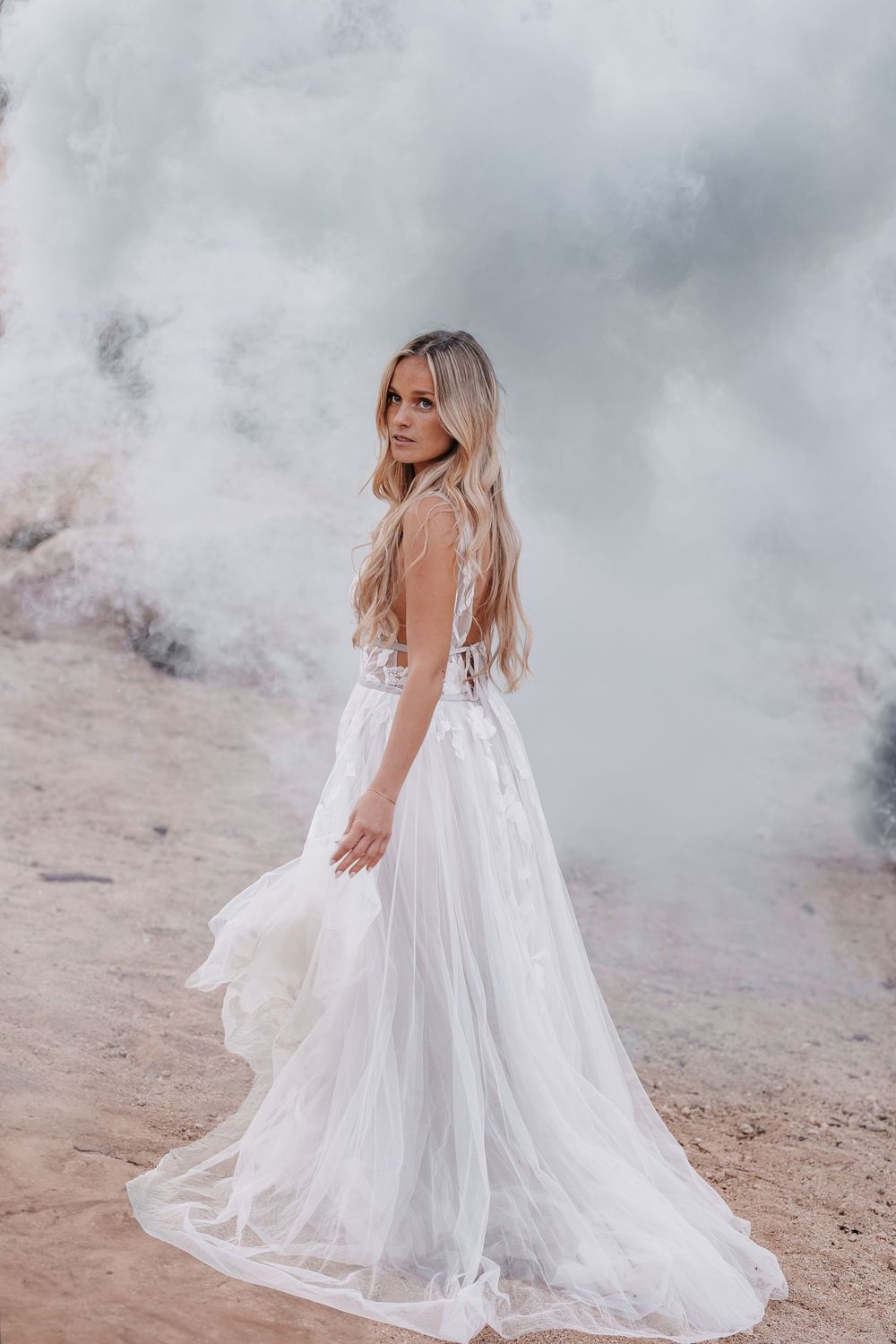 White flowing dress twirls against cloudy sky in ethereal bridal portrait.