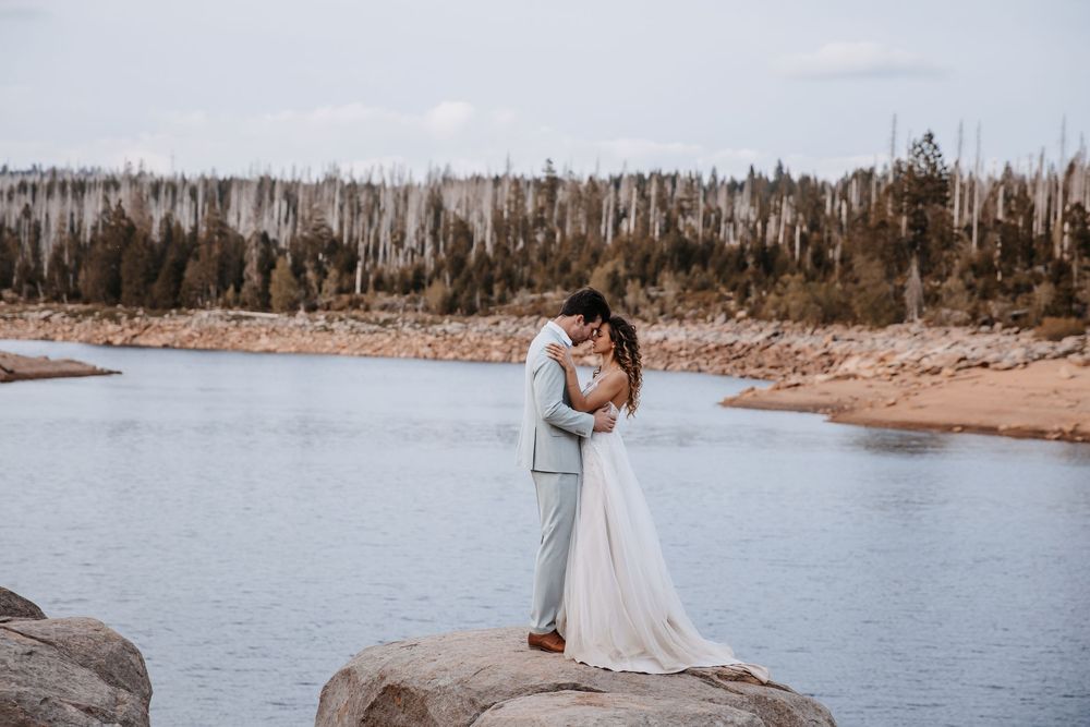 Newlyweds share an intimate moment by a serene lakeside setting at sunset.