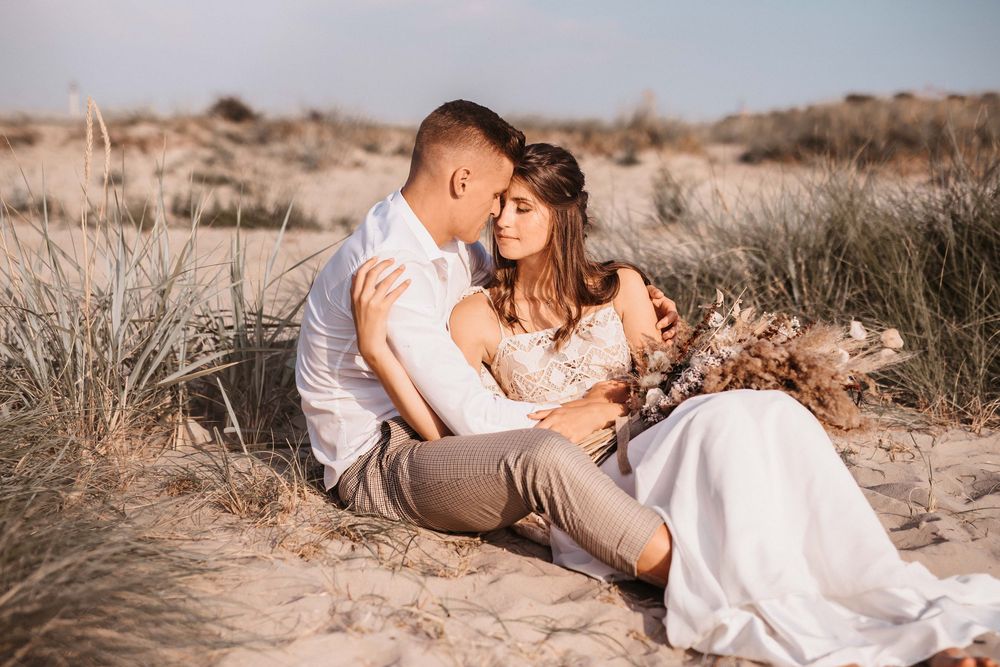 Couple shares romantic moments on sandy beach during sunset photoshoot.