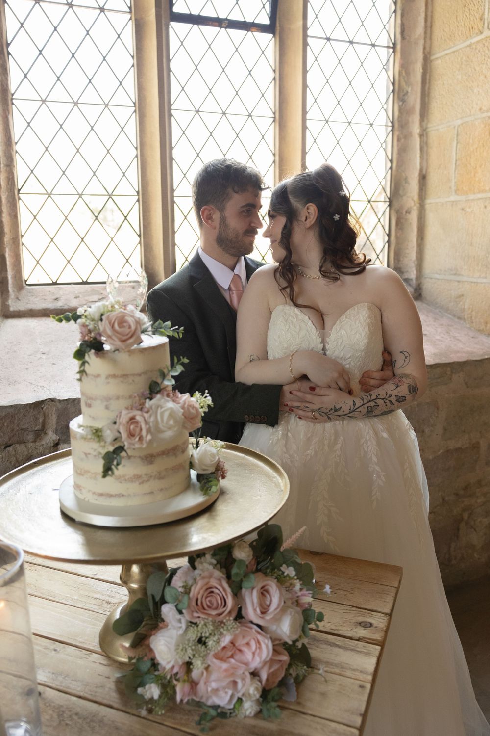 Wedding couple shares intimate moment while cutting elegant white and pink floral decorated cake at historic venue.