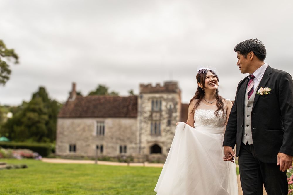 Couple in formal wedding attire walking and laughing together on castle grounds during their countryside celebration.