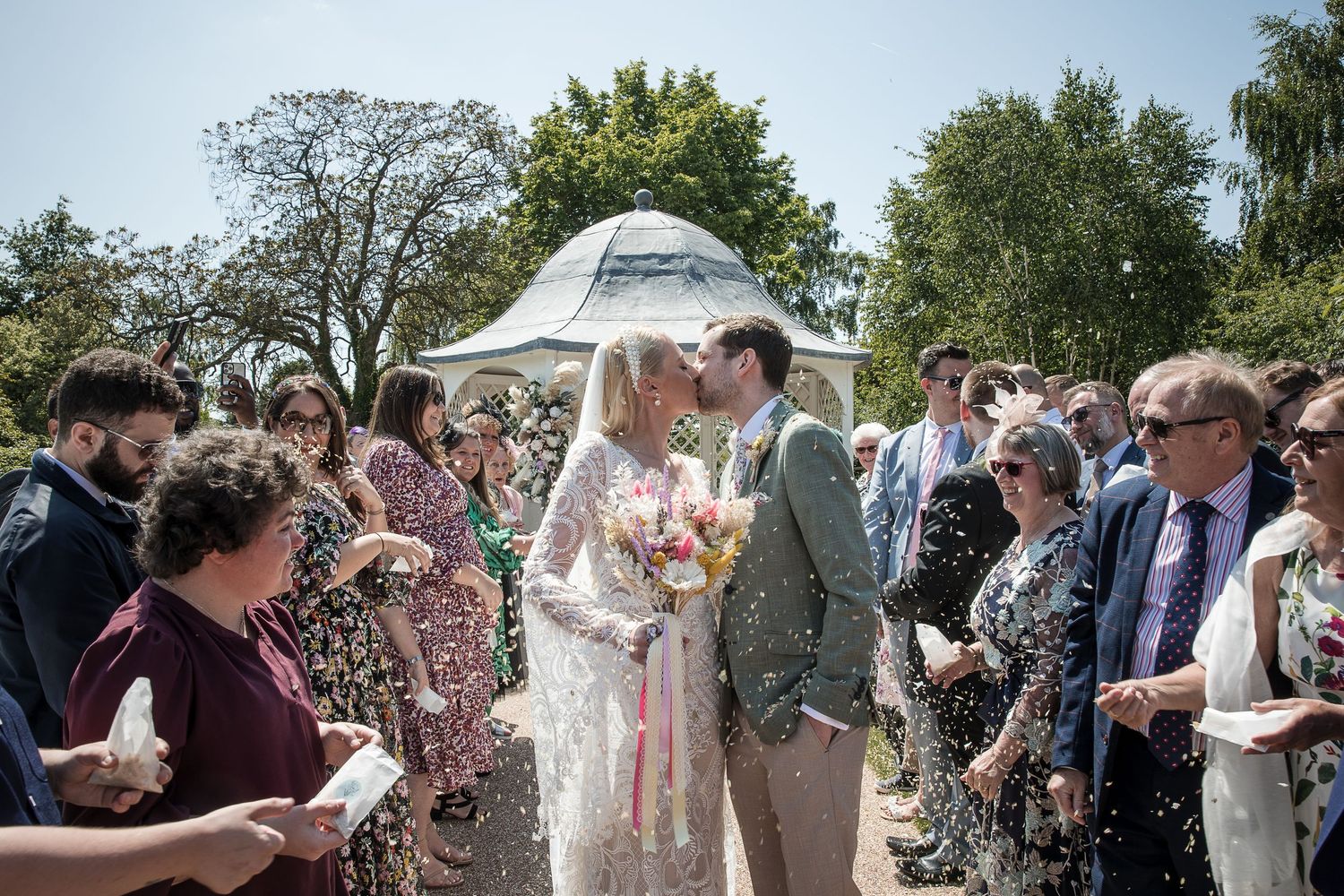Hodsock Priory bride and groom stop for a kiss as confetti fills the air after their vows at the gazebo