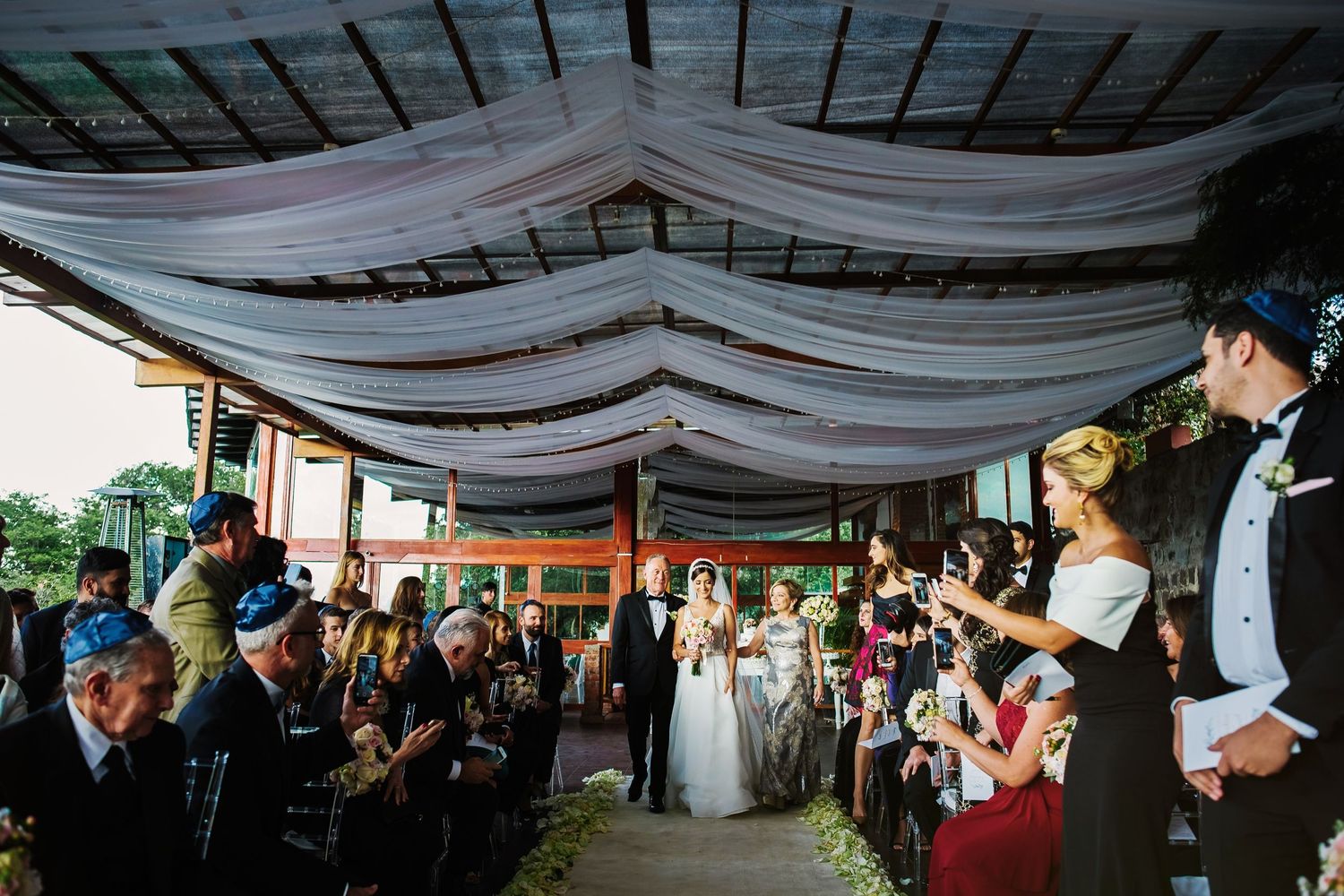 Wedding guests gathered under a draped canopy during an outdoor reception.