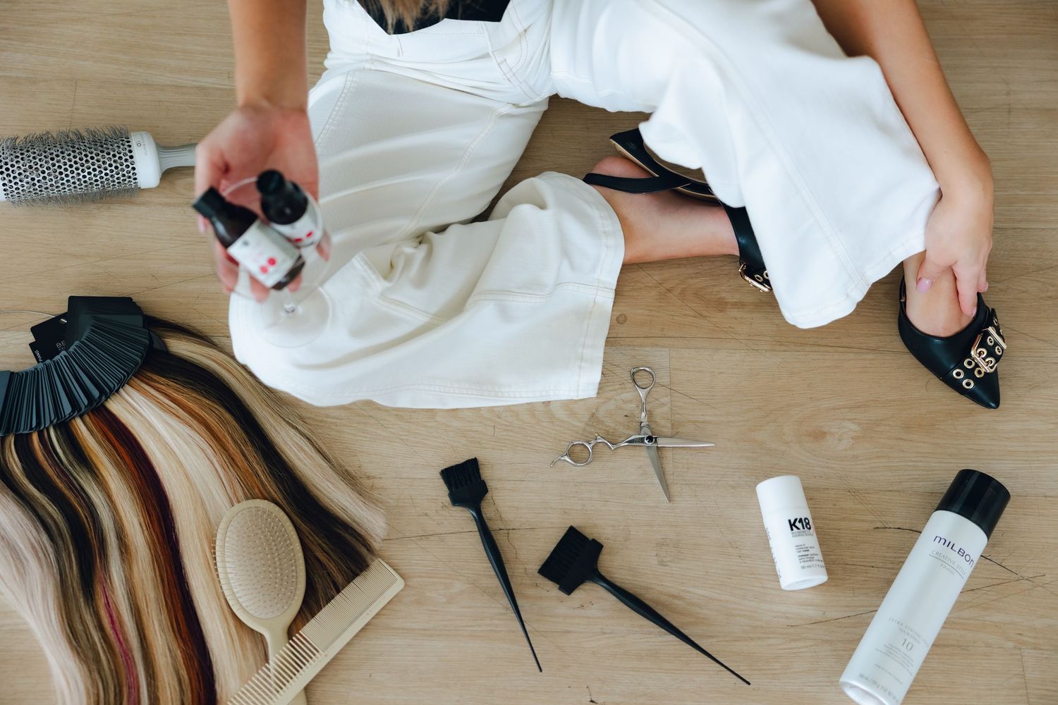 A series of hands shown styling and preparing clothing items and accessories on a wooden surface.
