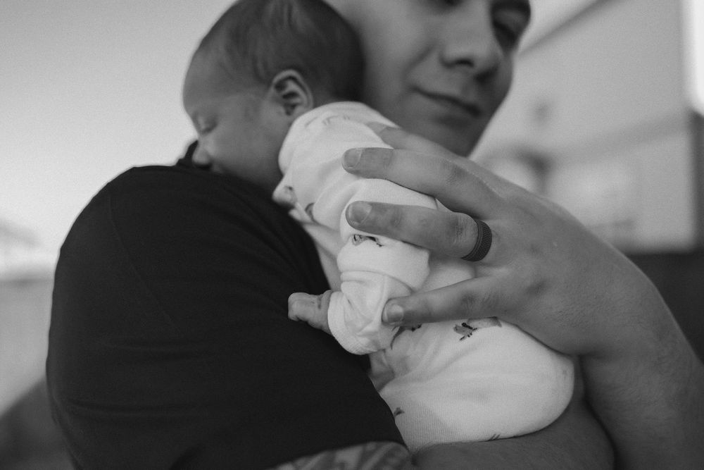 newborn baby sleeping on dads chest, his hand on their back, black and white photo