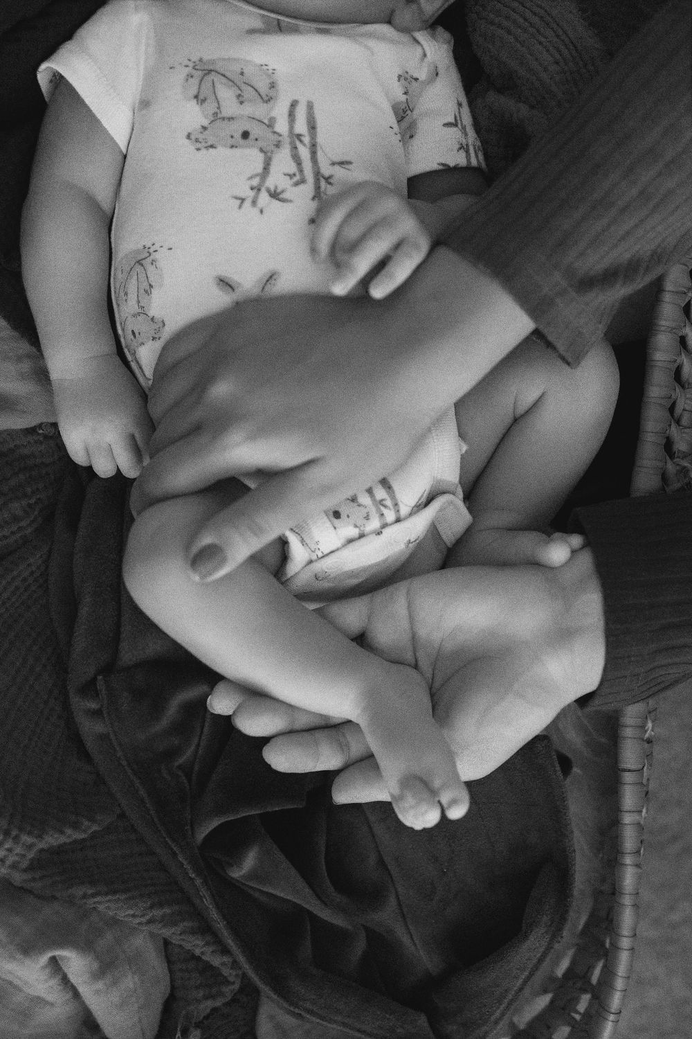 Black and white photo showing close-up details of a baby's hands and feet.  Females hands holding baby's feet