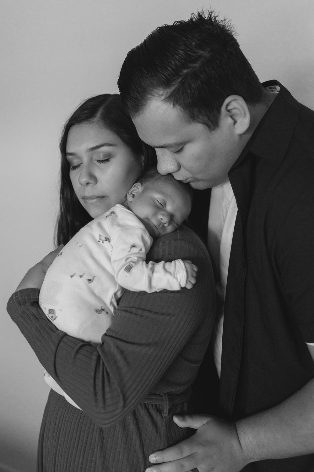 Black and white photo series showing tender moments between a couple holding their newborn baby.  Dad leaning over Moms shoulder