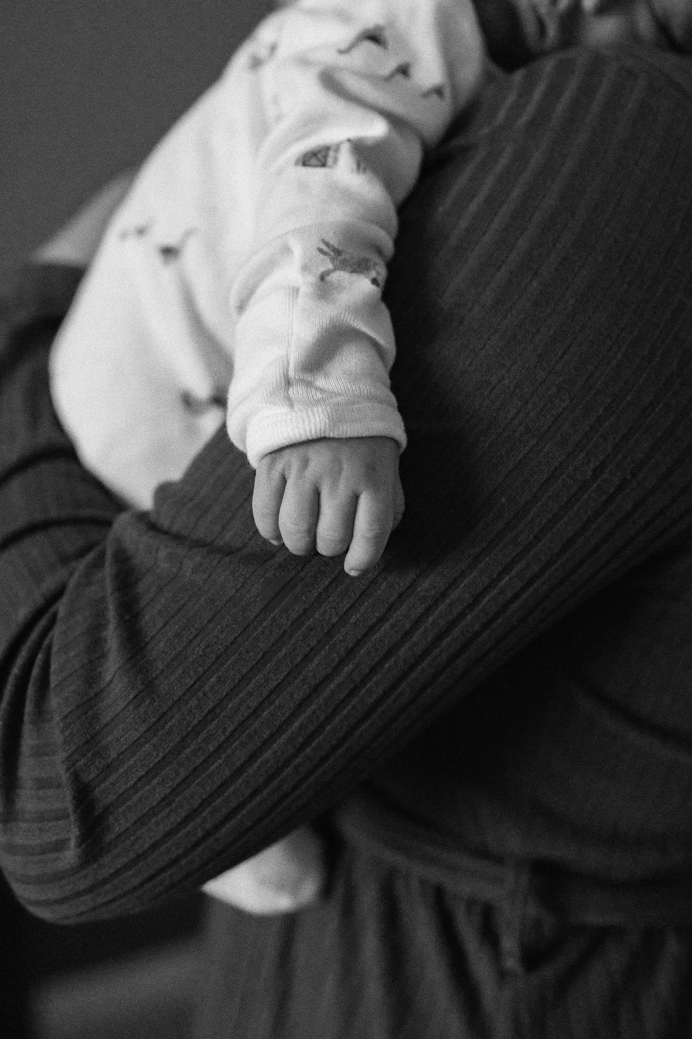 Black and white photoshowing close-up details of a baby's tiny hands and fingers against dark fabric.